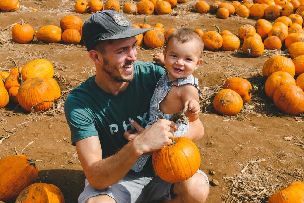 father holding his toddler son with pumpkins in patch surrounding them - photo by Derek Owens