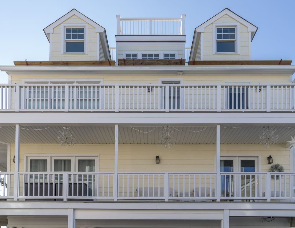 yellow 3 shory house exterior with 2 white balconies by raymond design build